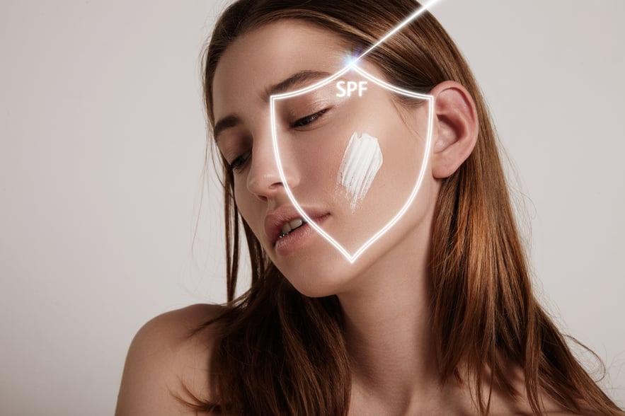 Young woman applying sunscreen cream with SPF protection graphic on face